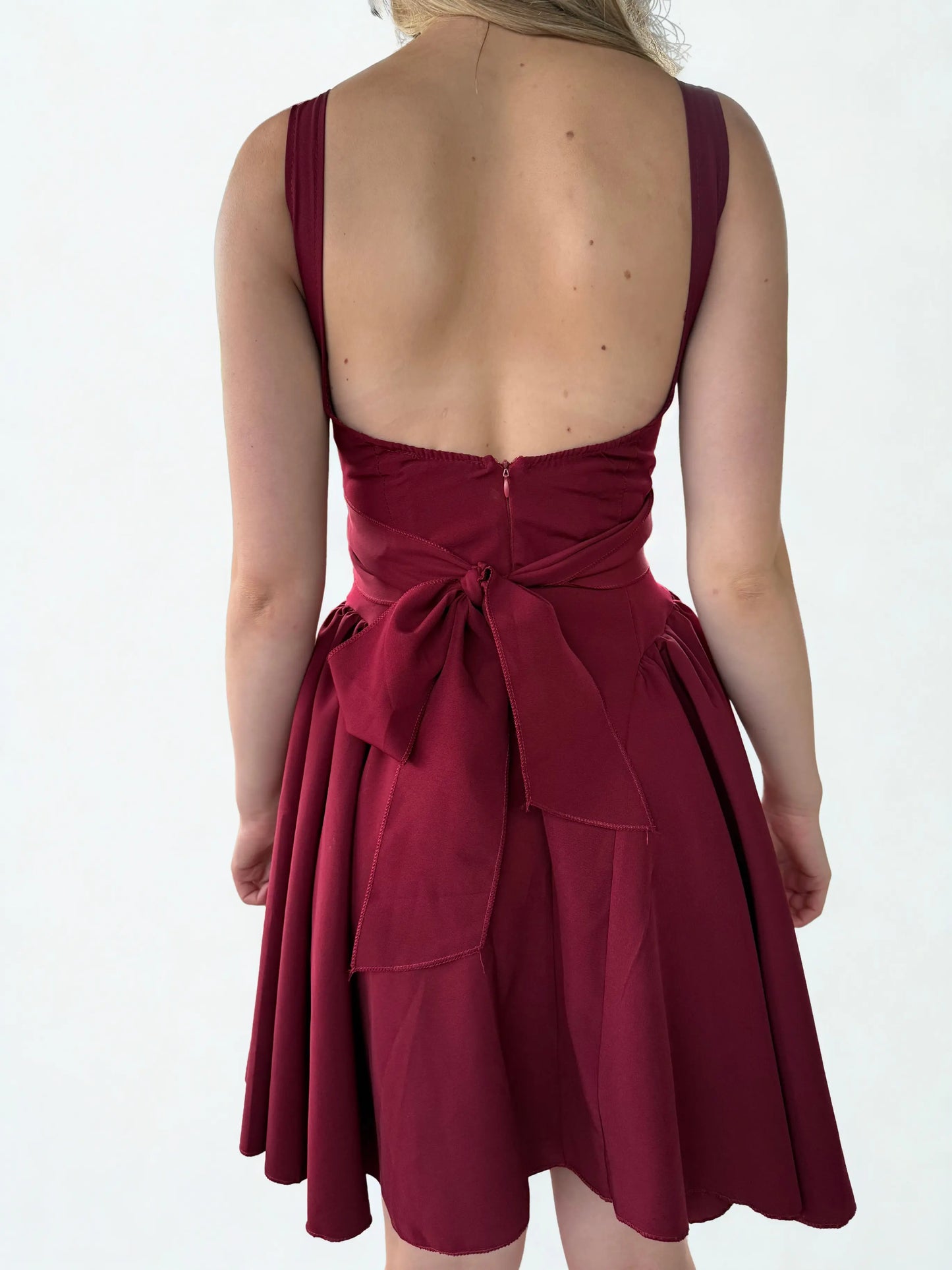 Achteraanzicht van een rode mini-jurk met een strakke pasvorm, lage rug en elegante lijnen die de vrouwelijke silhouet benadrukken.