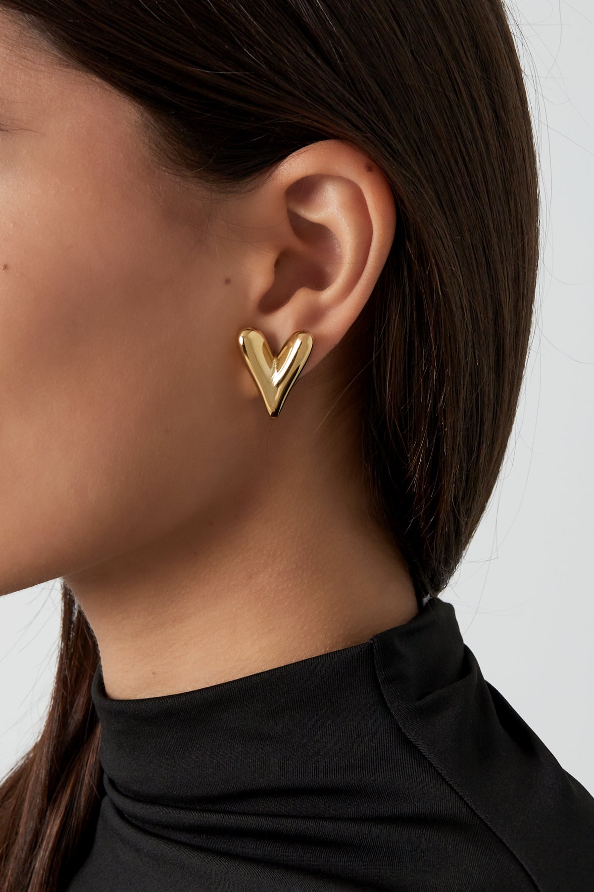 De goudkleurige hartvormige earstuds met een glanzende afwerking aan.