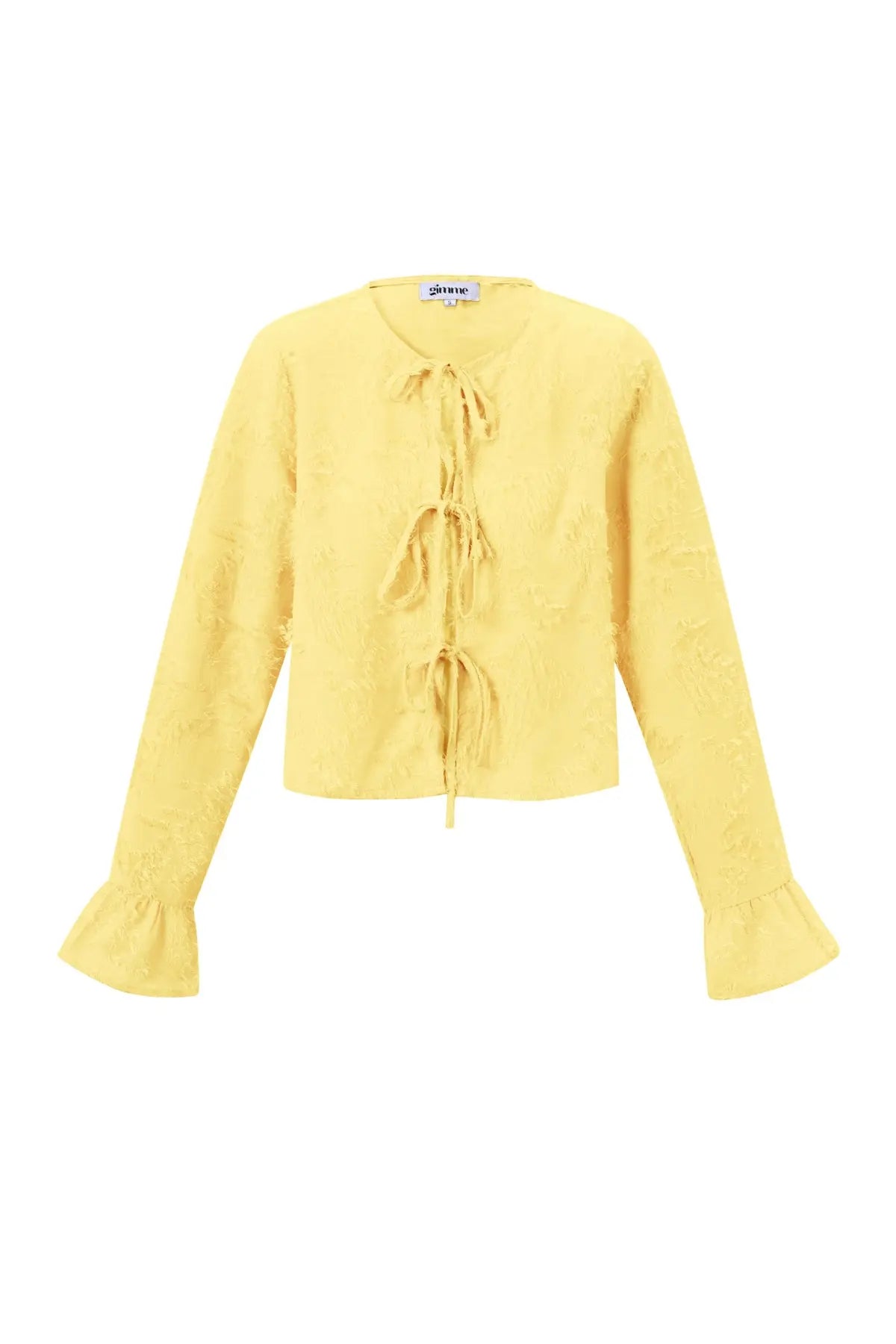 Voorkant lichtgele blouse met strikjes en textuur. Lange mouwen met licht uitlopende mouwen.