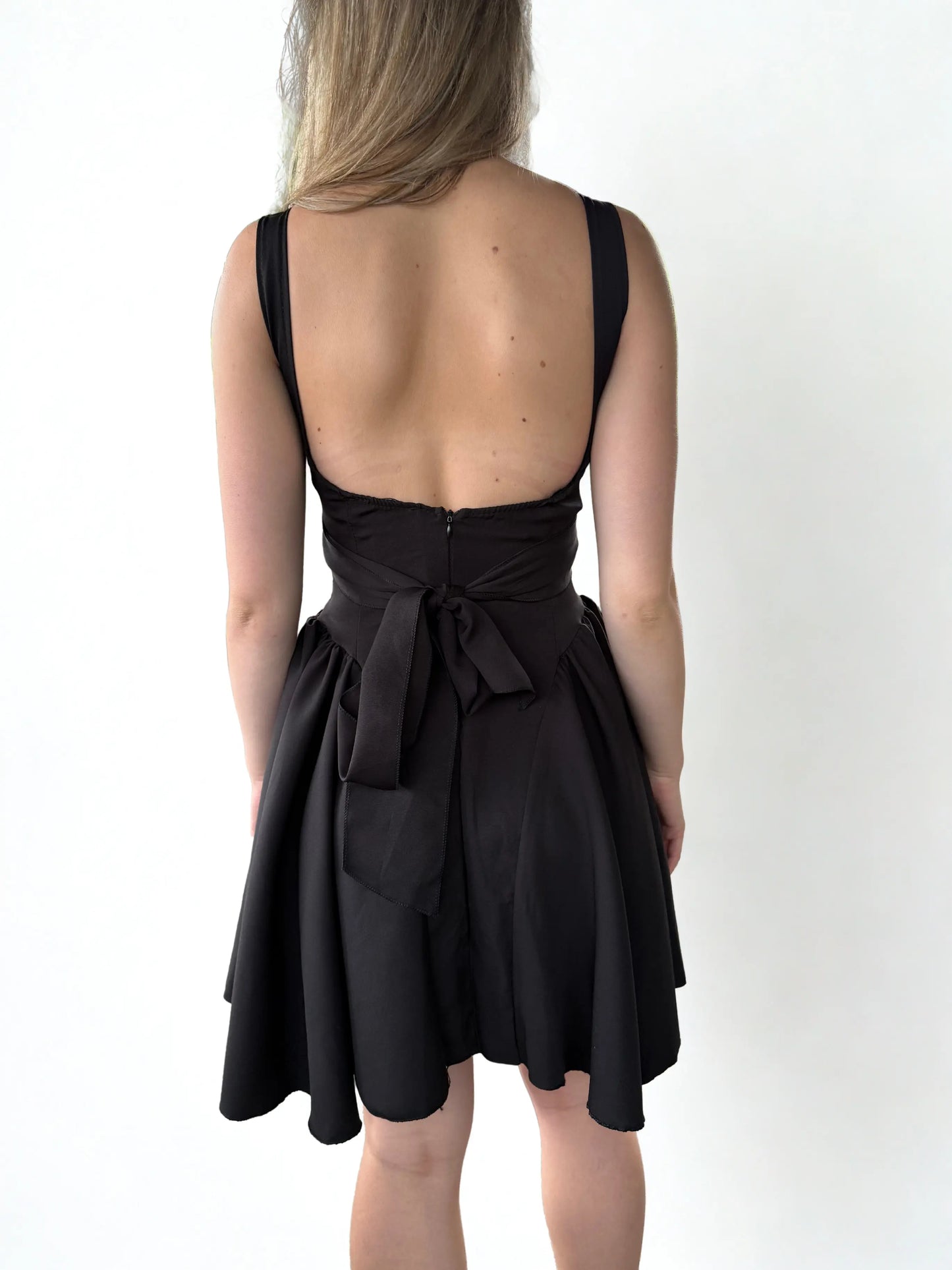 Achteraanzicht van een zwarte mini-jurk met een strakke pasvorm, lage rug en subtiele details voor een verfijnde, vrouwelijke look.